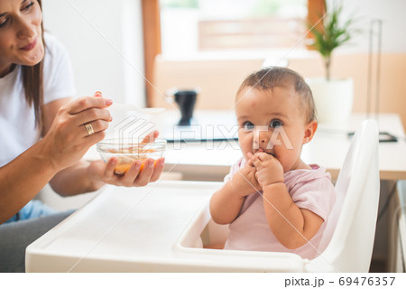 Funny adorable and dirty little baby girl of six months eats while sitting in the baby chair. 69476357