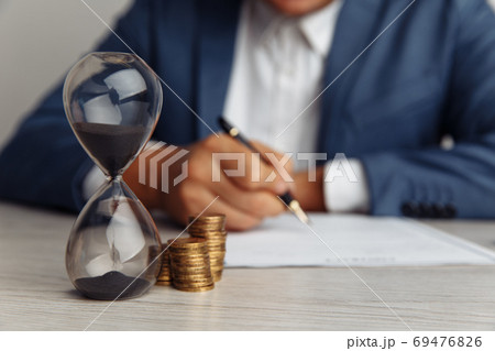 Businessman approves important contract in office. Stack of coins and hourglass on desk close-up. Time is money concept 69476826