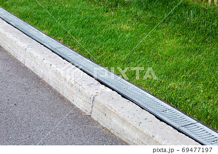drainage system along an asphalt road with a stone curb and grill for rainwater in a green lawn. drainage system along an asphalt road with a stone curb and grill for rainwater in a green lawn. 69477197