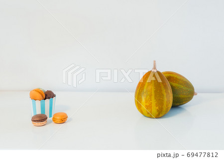 Minimalist Halloween concept - sweets, macarons dessert in a paper cup, and decorative pumpkins. Chocolate and pumpkin macaroons on a white background. Thanksgiving menu. Copy Space. Minimalist Halloween concept - sweets, macarons dessert in a paper cup, and decorative pumpkins. Chocolate and pumpkin macaroons on a white background. Thanksgiving menu. Copy Space. 69477812