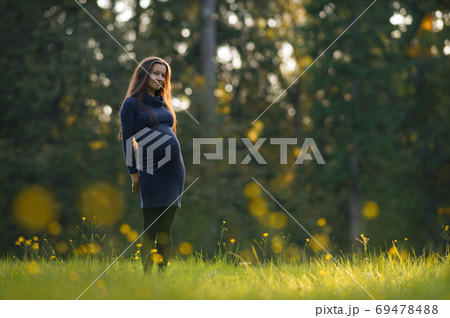 Young pregnant woman in dress standing on sunny meadow with yellow flowers in park. 9 months pregnancy. Expecting child 69478488