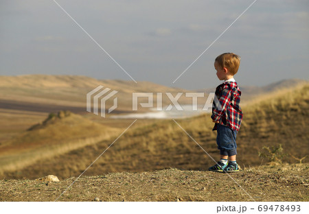 Side portrait of little boy standing lonely and looking into the distance in yellow desert field 69478493