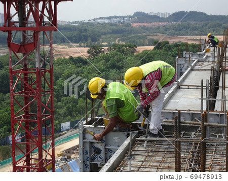 KUALA LUMPUR, MALAYSIA -MAY 05, 2016: Construction workers wearing a safety harness and adequate safety gear when climbing the scaffolding. This is to ensure their safety while working at a high level KUALA LUMPUR, MALAYSIA -MAY 05, 2016: Construction workers wearing a safety harness and adequate safety gear when climbing the scaffolding. This is to ensure their safety while working at a high level 69478913