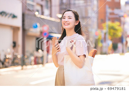 街中でスマホを持つ買い物帰りの若い女性 69479181