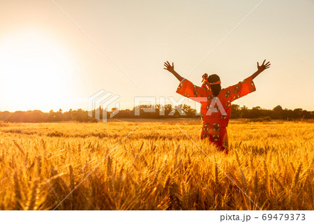 African woman in traditional clothes standing arms raised in field sunset or sunrise 69479373