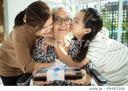 Happy asian mother,daughter meeting old grandparent,giving grandmother a gift,hugging,female elderly hold  present box,woman,child girl visiting senior mother,receiving kisses in cheek from her family 69485366