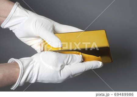 Men's hand in white gloves holding a gold bullion Men's hand in white gloves holding a gold bullion 69489986