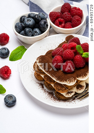 portion of Classic tiramisu dessert with raspberries and blueberries on ceramic plate isolated on white portion of Classic tiramisu dessert with raspberries and blueberries on ceramic plate isolated on white 69495729