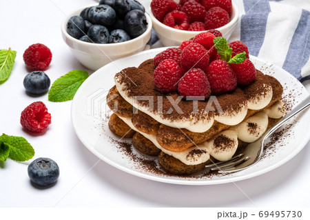 portion of Classic tiramisu dessert with raspberries and blueberries on ceramic plate isolated on white portion of Classic tiramisu dessert with raspberries and blueberries on ceramic plate isolated on white 69495730