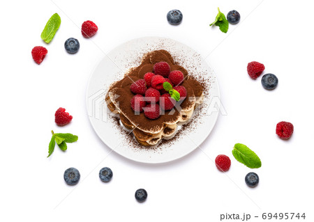 portion of Classic tiramisu dessert with raspberries and blueberries on ceramic plate isolated on white 69495744