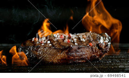 Tasty beef steak on cast iron grate with fire flames. Tasty beef steak on cast iron grate with fire flames. 69498541