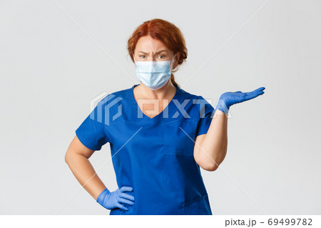 Medical workers, covid-19 pandemic, coronavirus concept. Confused skeptical female doctor, dentist in scrubs, face mask and gloves, shrugging, pointing right and frowning disappointed Medical workers, covid-19 pandemic, coronavirus concept. Confused skeptical female doctor, dentist in scrubs, face mask and gloves, shrugging, pointing right and frowning disappointed 69499782