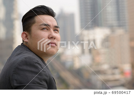 Closeup profile view of young overweight Asian businessman thinking in the city 69500417