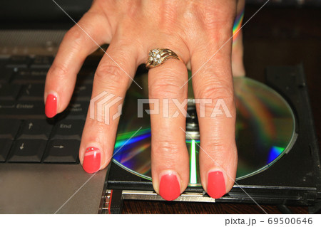 woman's hand with red nails taking DVD disc from PC. woman's hand with red nails taking DVD disc from PC. 69500646
