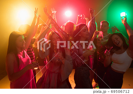 A crowd of people in silhouette raises their hands on dancefloor on neon light background 69506712