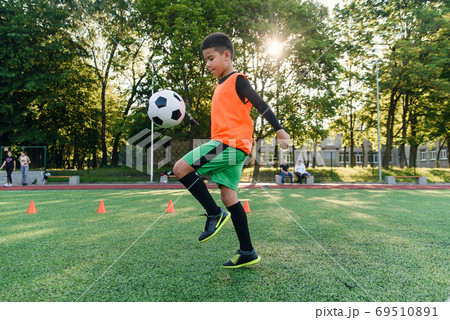 Focused skillful teen football player stuffs soccer ball on leg. Practicing sport exercises at artificial stadium. Focused skillful teen football player stuffs soccer ball on leg. Practicing sport exercises at artificial stadium. 69510891