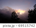 The sun rises and breaks through the clouds over the forest creating silhouettes of coniferous trees 69515742