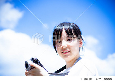青空をバックにカメラを構える若い女性 69516006