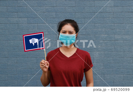 Masked woman in brown shirt and Wyoming flag in hand. 69520099