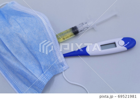 Focus on medical mask.Syringe, protective mask and electronic thermometer on a grey background.Vaccination against the virus. Focus on medical mask.Syringe, protective mask and electronic thermometer on a grey background.Vaccination against the virus. 69521981