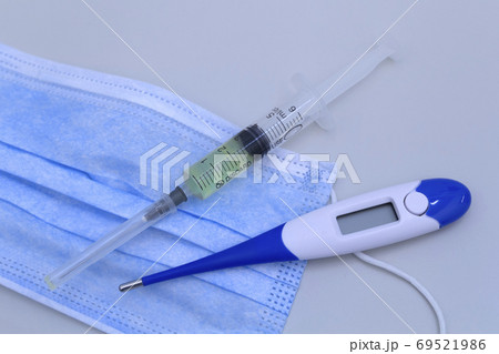 Syringe, protective mask and electronic thermometer on a grey background.Vaccination against the virus. 69521986