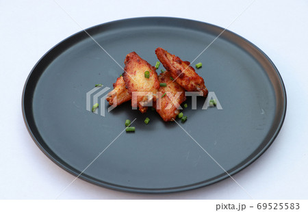 Grilled chicken wings in the black round plate on the white floor. 69525583