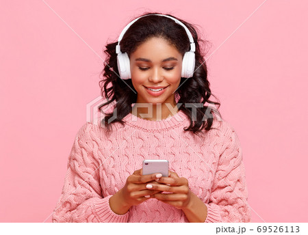 Cheerful ethnic woman listening to music and using smartphone. Cheerful ethnic woman listening to music and using smartphone. 69526113