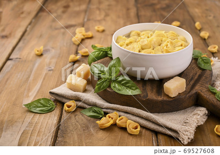 Tortellini mignon on a wooden board with basil and parmesan. Specialties of the cuisine from Bologna 69527608