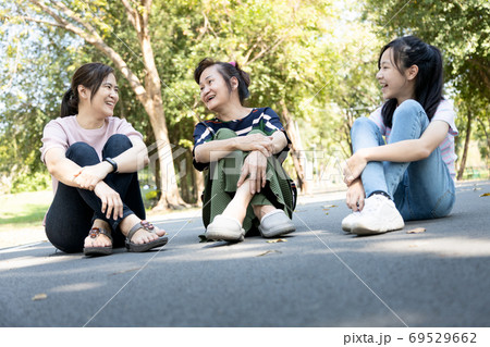 Smiling happy asian family spending good time at the park together,enjoying in outdoor summer nature,joyful grandmother,daughter and granddaughter sitting on the floor,relax,laugh,talk fun in garden  69529662