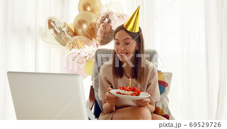 Woman blows out candle on cake in front of laptop Woman blows out candle on cake in front of laptop 69529726