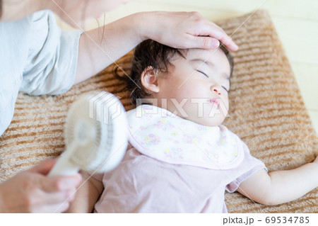 真夏 寝ている赤ちゃんにハンディ扇風機を当てる母の手の写真素材