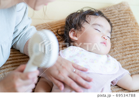 真夏　寝ている赤ちゃんにハンディ扇風機を当てる母の手 69534788