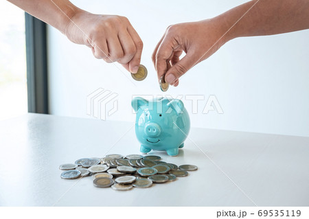 Image of hands putting coins into piggy bank 69535119