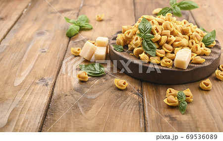 Tortellini mignon on a wooden board with basil and parmesan. Specialties of the cuisine from Bologna Tortellini mignon on a wooden board with basil and parmesan. Specialties of the cuisine from Bologna 69536089