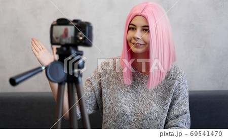 Happy girl blogger in pink wig in front of the camera on a tripod Happy girl blogger in pink wig in front of the camera on a tripod 69541470