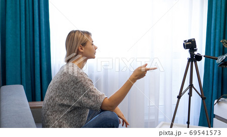 Young woman in casual clothes records herself on camera on tripod. Side view 69541573
