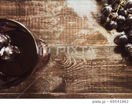 A bunch of grapes in an old vase and in glass for wine with wine a glass of wine on a wooden table . 69541662