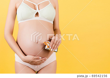 Cropped image of a pack of cigarettes at yellow background. Bad habbit of a pregnant woman in colorful underwear. Careless mother Cropped image of a pack of cigarettes at yellow background. Bad habbit of a pregnant woman in colorful underwear. Careless mother 69542156