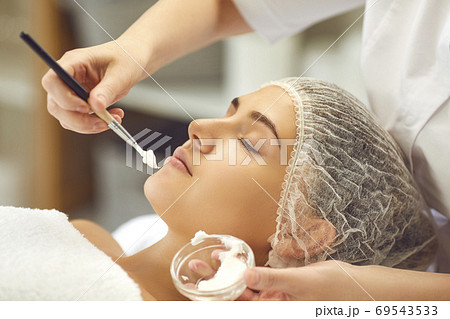 Hands of dermatologist putting moisturizing cream to womans face during skincare procedure in spa salon Hands of dermatologist putting moisturizing cream to womans face during skincare procedure in spa salon 69543533