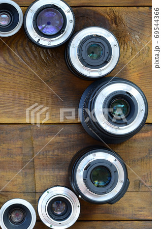 Several photographic lenses lie on a brown wooden background. Sp 69544366