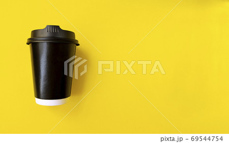 Black paper coffee cup to go on a yellow backgroud. Simple flat lay with copy space. Minimal concept. Stock photo. 69544754