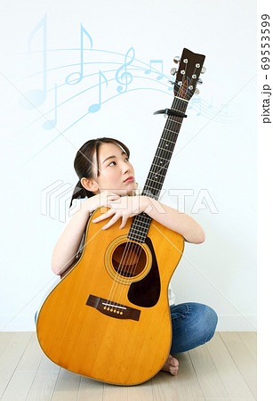 流れる音符とアコースティックギターを持つ若い女性イメージの写真素材