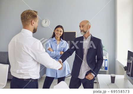 Friendly male company manager and aged client shaking hands confirming a business deal Friendly male company manager and aged client shaking hands confirming a business deal 69558573