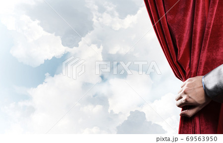 Cloudy landscape behind red curtain and hand holding it Cloudy landscape behind red curtain and hand holding it 69563950