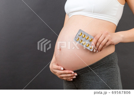 Cropped image of pregnant woman holding a blister of pills against her belly at colorful background with copy space. Nutritional supplement concept 69567806