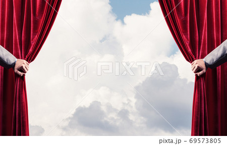 Cloudy landscape behind red curtain and hand holding it Cloudy landscape behind red curtain and hand holding it 69573805
