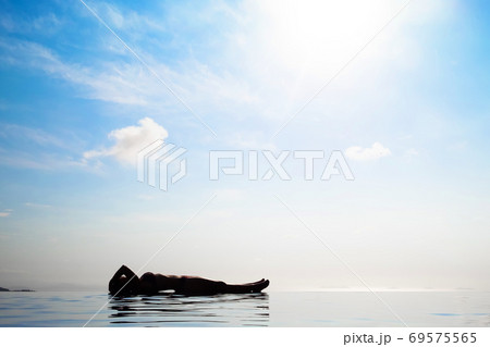 Woman relaxing in infinity swimming pool looking at view 69575565