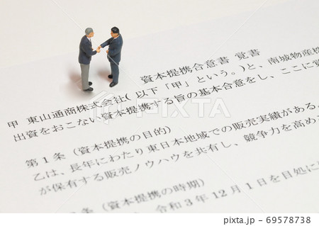 資本提携合意書の上で握手しようとしているビジネスマンのミニチュア 69578738
