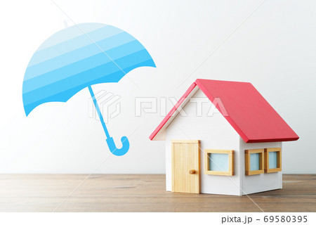 住宅の保険。家のミニチュアと傘のイラスト。木のテーブルと白い背景。 住宅の保険。家のミニチュアと傘のイラスト。木のテーブルと白い背景。 69580395