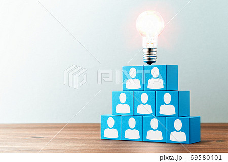 チームワークと創造性のイメージ。木のテーブルの上の人のアイコンが描かれた青い積木と電球。 69580401